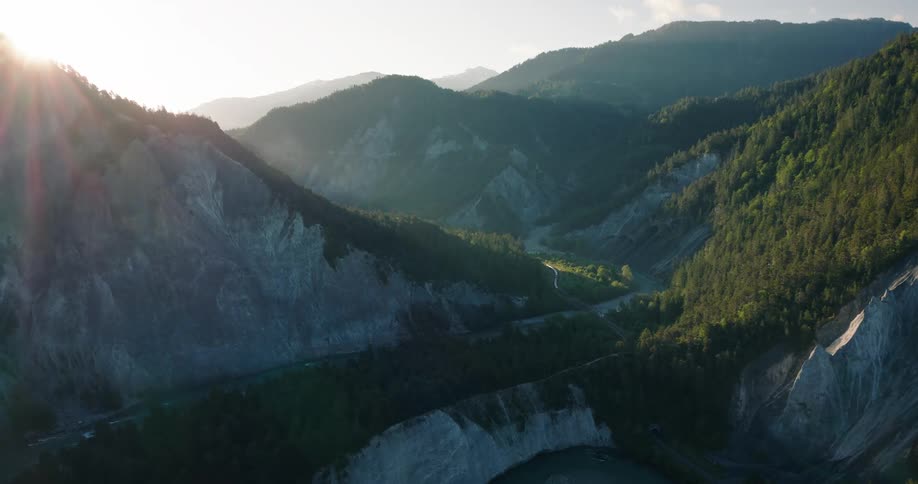 Epic aerial footage captures the sun rising over a dramatic mountain gorge with a river snaking through the valley floor