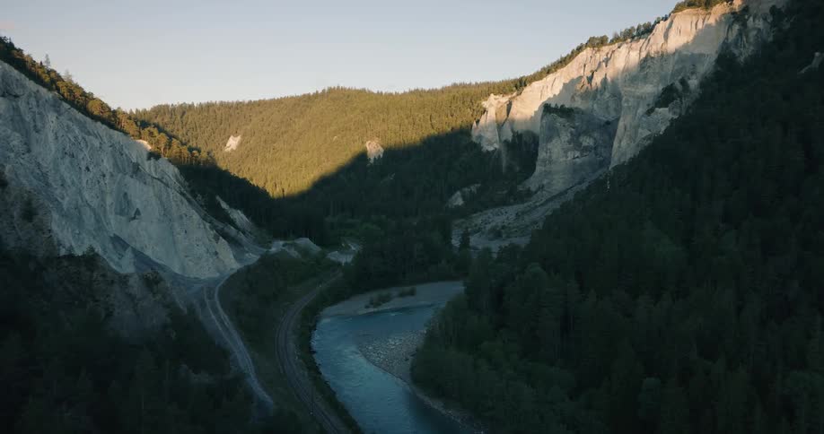 An awe-inspiring aerial view of a river winding through a majestic gorge with sunlit cliffs and shadowed forests at sunrise