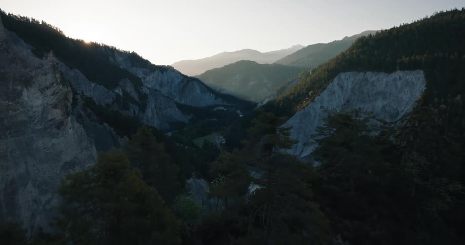 Cinematic aerial pulls back over a majestic mountain canyon as the sun rises, revealing a river snaking through the forested valley below