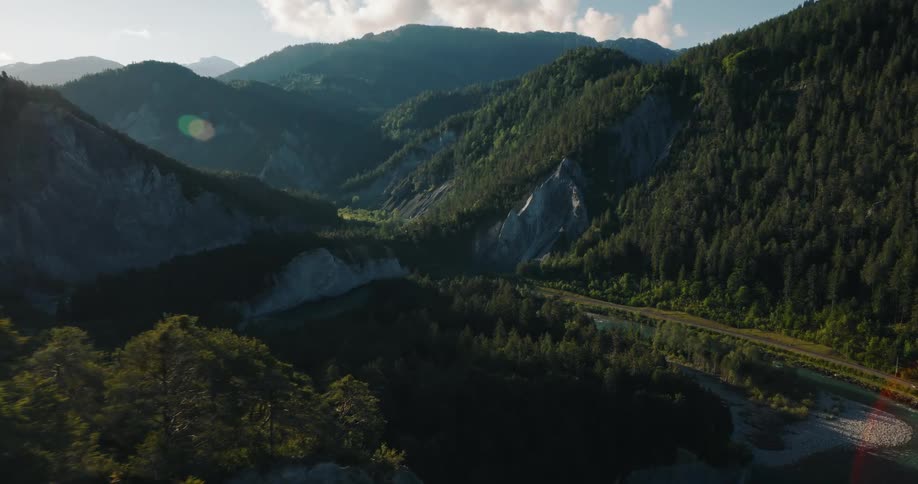 Cinematic aerial shot flying over a dramatic mountain valley with a winding river and dense forests at golden hour