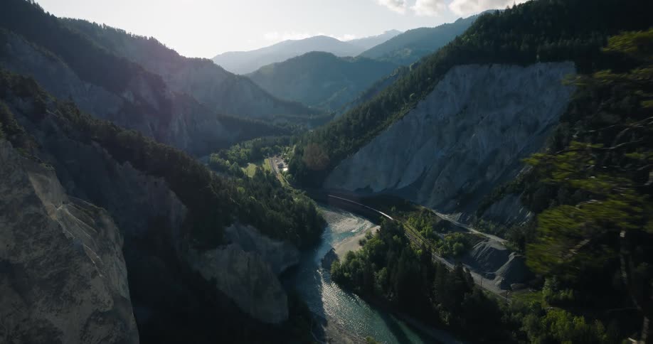 A cinematic aerial shot pushing past evergreen trees reveals a stunning mountain valley with a river winding through it at sunrise
