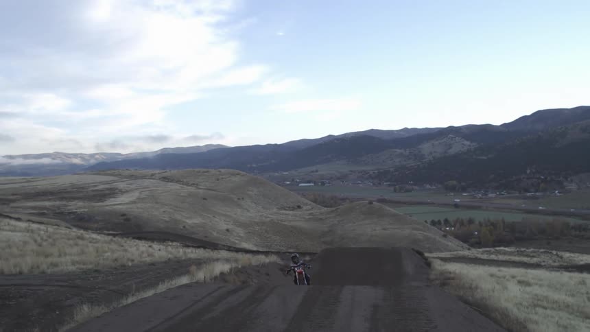 A motocross rider sits on their dirt bike at the top of a ramp overlooking a scenic mountain valley