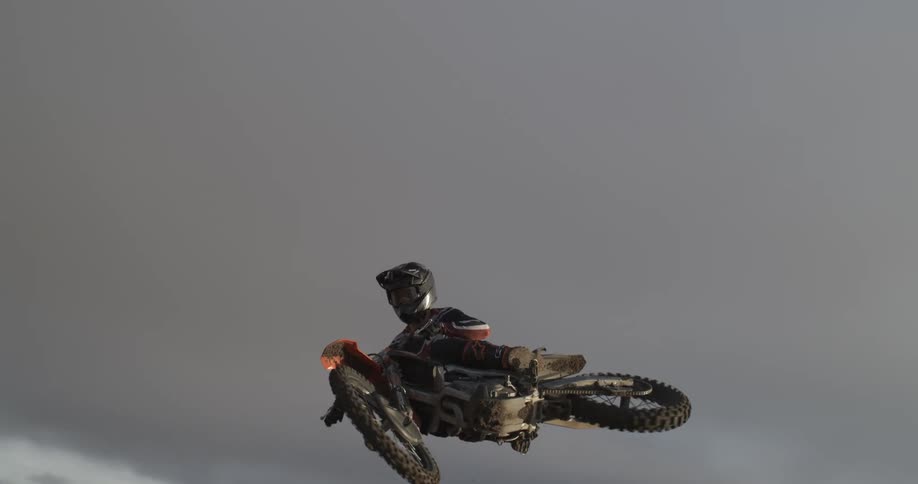 Dramatic slow motion shot of a motocross rider suspended mid-air against a gloomy gray sky