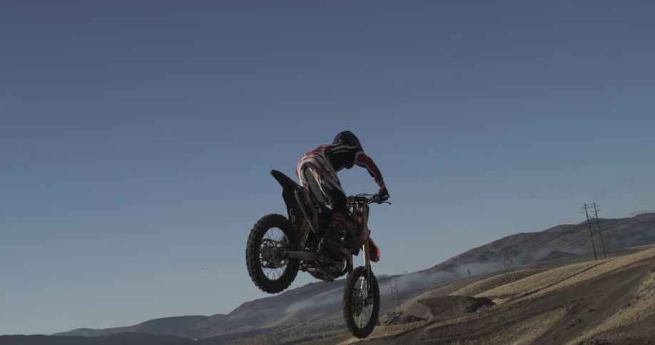 A motocross rider is frozen in mid-air while performing a jump on a dirt bike in slow motion