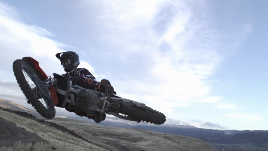 A futuristic speeder bike rider soars through the air in dramatic slow motion over a vast canyon landscape