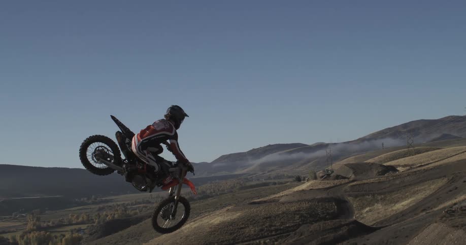 An extreme motocross rider hangs suspended in mid-air over a vast mountain landscape after launching off a jump in super slow motion