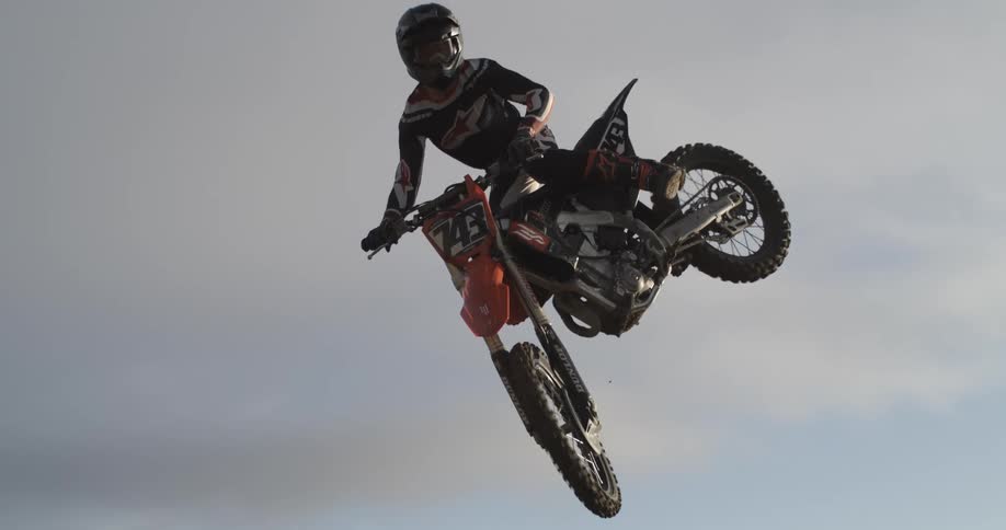 An extreme motocross rider performs a big air jump and whip trick in stunning super slow motion