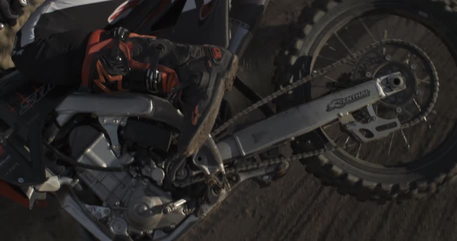 A slow motion shot tilts down from the sky to reveal a motocross rider on their dirt bike in the mountains