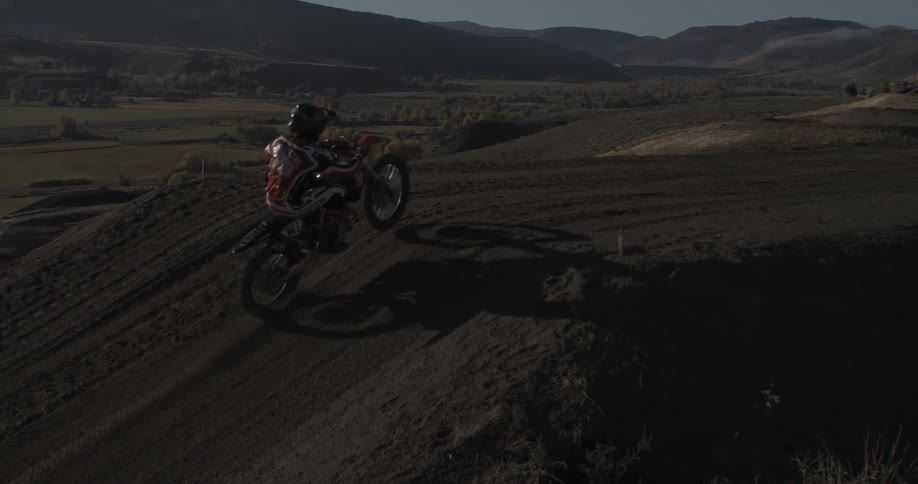 A motocross rider in slow motion performs a dramatic jump off a dirt ramp in the scenic countryside at sunrise