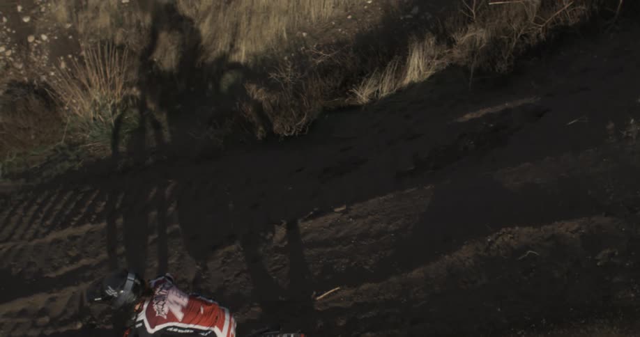 A motocross racer rides a dirt bike around a corner on a dirt track in slow motion, shot from a high angle