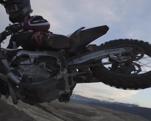 A motocross rider soars through the air in extreme slow motion against a backdrop of rolling hills and a dusky sky