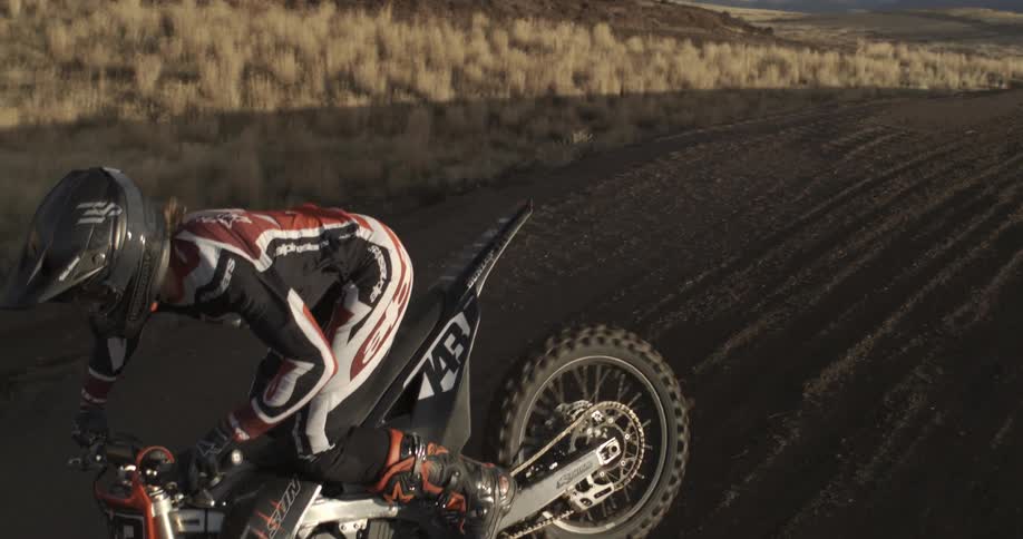 A motocross rider in full gear skillfully navigates down a dirt hill in dramatic slow motion during golden hour