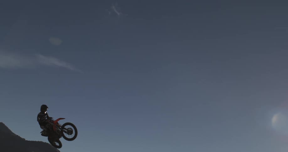 In dramatic slow motion, a motocross rider on a dirt bike soars through the air after launching off a steep mountain hill