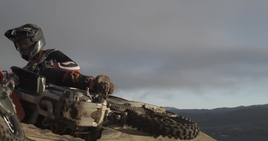 A motocross rider jumps a dirt bike off a hill in dramatic super slow motion against a vast landscape