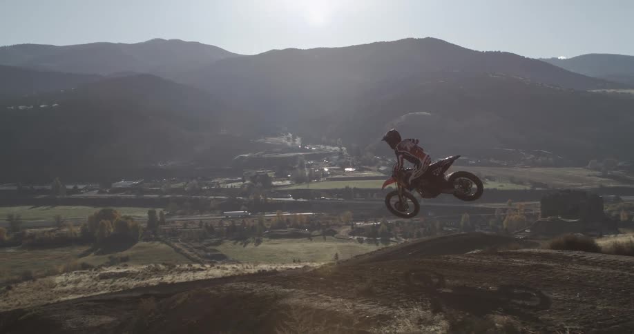 Epic super slow motion shot of a motocross rider getting huge air and performing a stylish whip trick with a scenic valley in the background