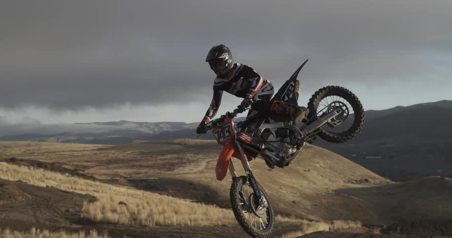 A motocross rider performs a spectacular jump, hanging suspended in the air in dramatic super slow motion over a vast hilly terrain