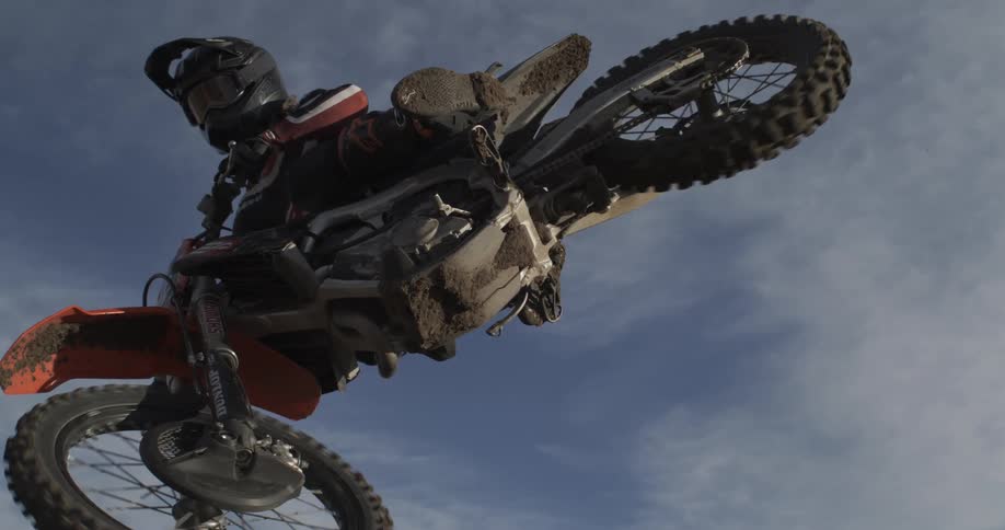 An extreme motocross rider performs a huge jump, captured in super slow motion from a dramatic low angle