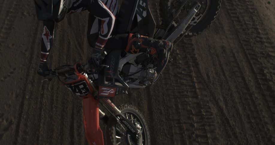 A professional motocross rider performs a whip trick mid-air in super slow motion on a dirt track in the mountains