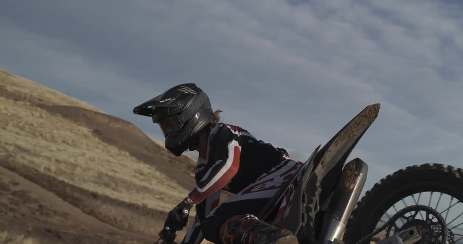 A motocross rider gracefully lands a jump in extreme slow motion on a dirt track in the hills