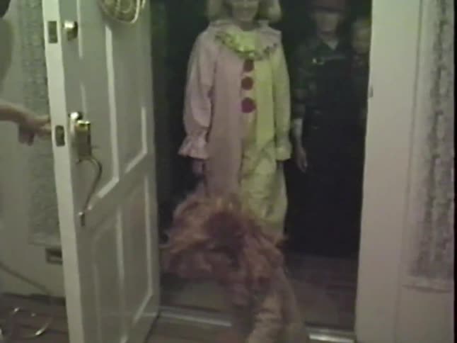 A vintage home video shows excited children in Halloween costumes roaring and laughing as they are let inside a house