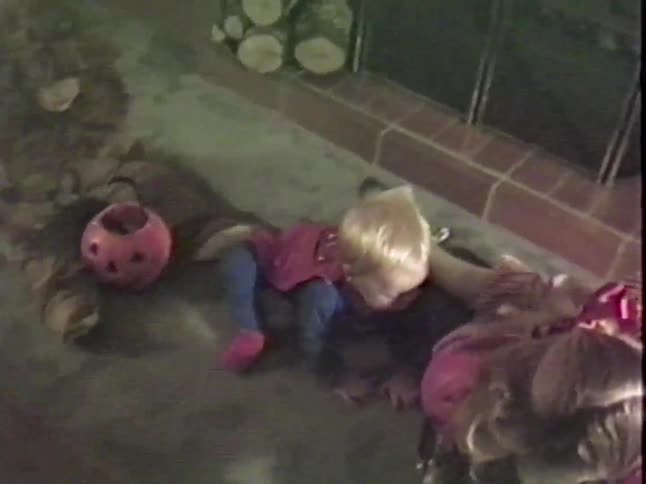 Vintage VHS footage shows a baby and a young girl playing with their Halloween jack-o'-lantern candy buckets on the floor