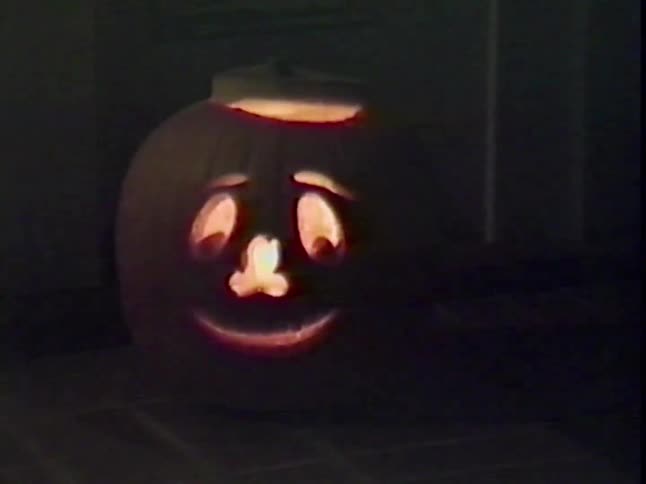 A slow zoom out of a glowing jack-o'-lantern with a friendly face sitting on the front porch on a dark Halloween night