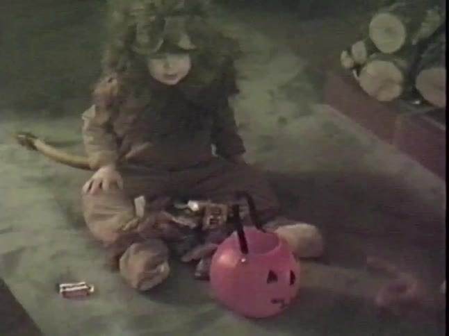 A cute toddler in a lion costume sits on the floor and happily sorts through their Halloween candy haul