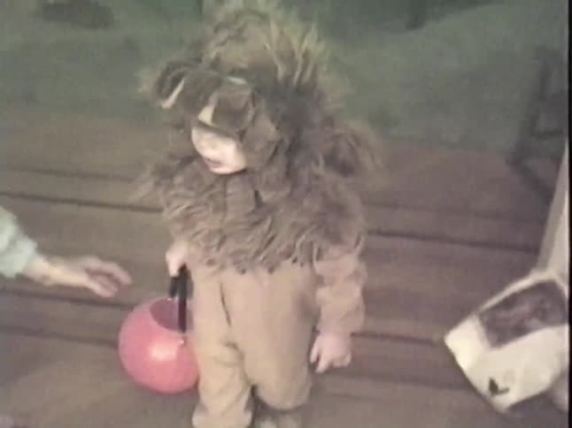 A cute toddler in a lion costume holds a pink jack-o'-lantern bucket, getting ready for Halloween in this vintage home video