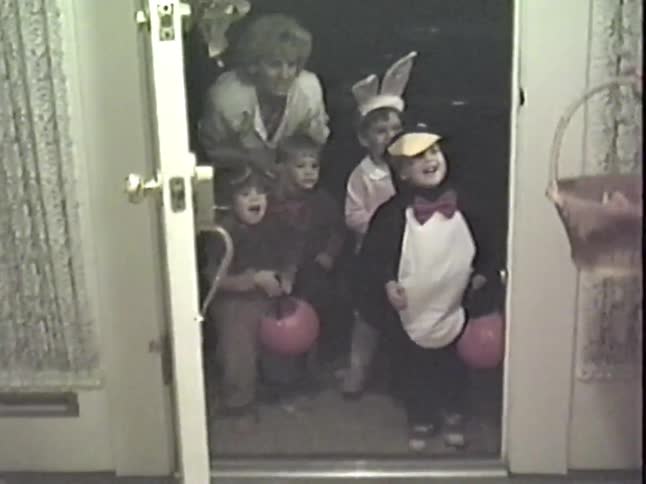 Vintage home video captures a group of adorable children in costumes trick-or-treating on Halloween night