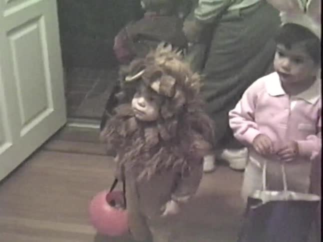 An adorable toddler dressed as a lion with a pink candy bucket gets ready to go trick-or-treating with friends in this vintage home video