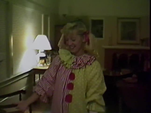 A woman in a clown costume laughs and dances before picking up a child in a lion costume for Halloween