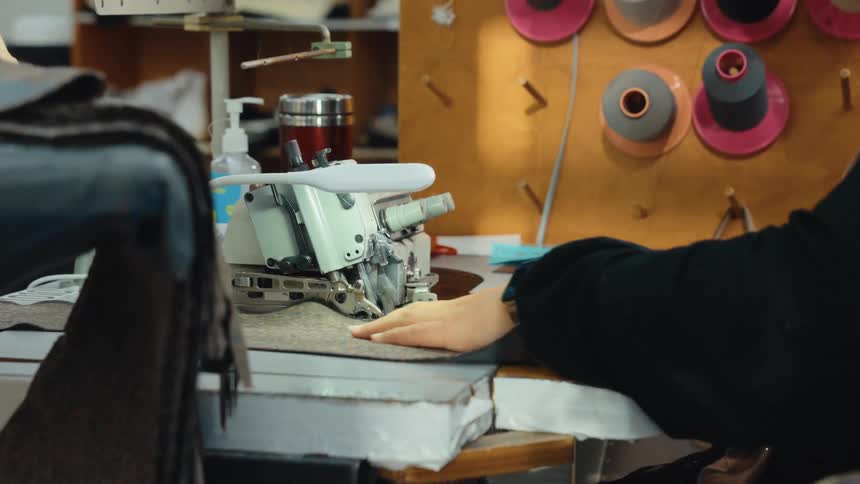 Closeup of a worker operating an industrial overlock sewing machine in a textile factory