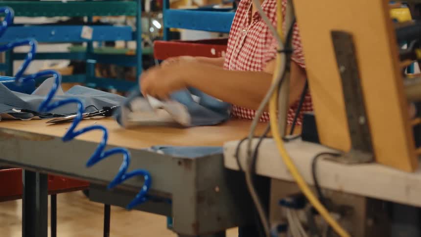 A factory worker carefully cuts a piece of blue fabric with scissors at her workstation