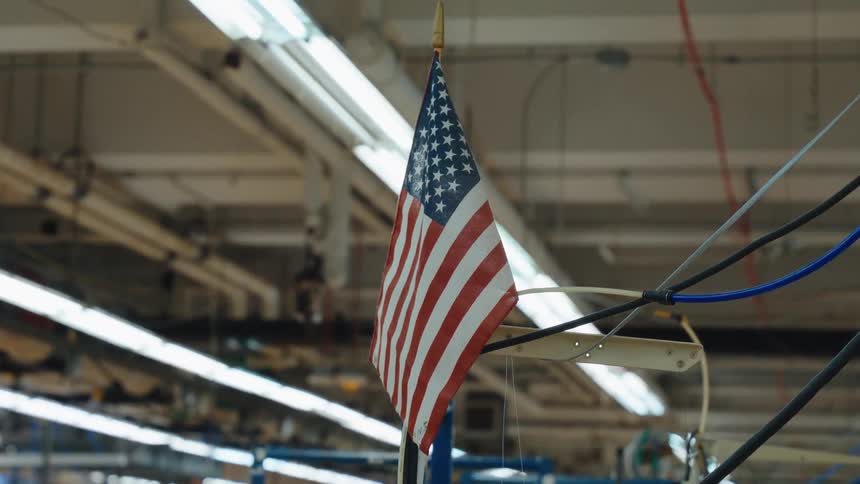 An American flag hangs from the ceiling of a large industrial factory with a slow zoom