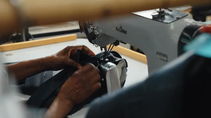 Close-up of a skilled tailor's hands meticulously sewing black fabric on a vintage sewing machine in a workshop