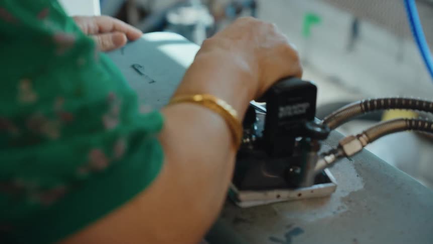 A close-up shot of a garment factory worker's hands as they meticulously press a piece of fabric with an industrial steam iron