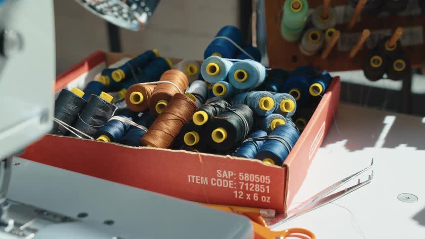 A box of colorful thread spools sits on a tailor's workbench next to a sewing machine
