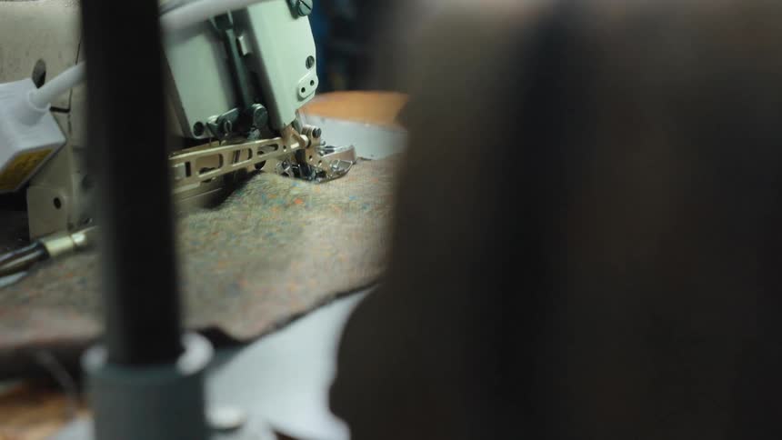 A close up over-the-shoulder perspective of a seamstress operating an industrial sewing machine