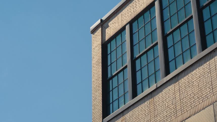 Slow zoom on the corner of a modern brick building with large windows against a clear blue sky