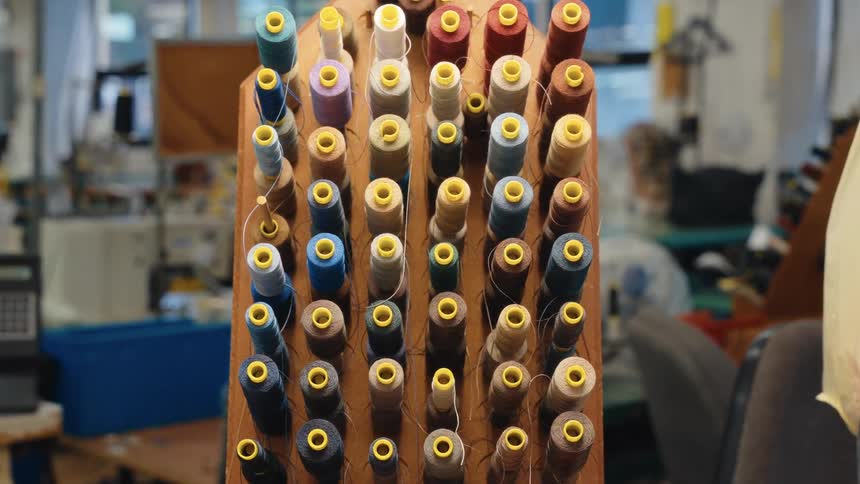 A slow zoom shot showcases a wooden rack filled with vibrant spools of thread in a bustling sewing factory