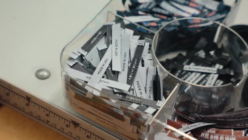 A close-up shot of a container filled with 'Made in USA' clothing labels on a workbench in a garment factory
