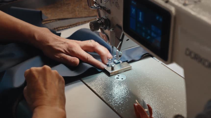 Close-up of a seamstress's hands carefully guiding dark blue fabric through a modern industrial sewing machine