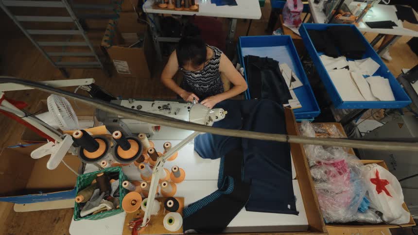 High angle shot of a female garment worker operating an industrial sewing machine in a busy factory