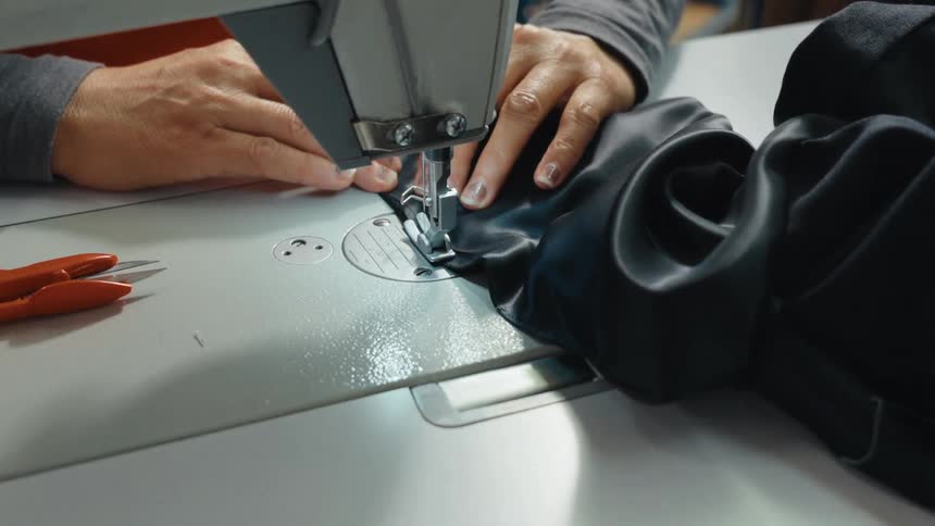 Close-up shot of a skilled seamstress using an industrial sewing machine to stitch a piece of black fabric