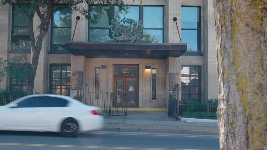 A slow zoom on an official-looking brick building with a coat of arms as traffic passes by on the street