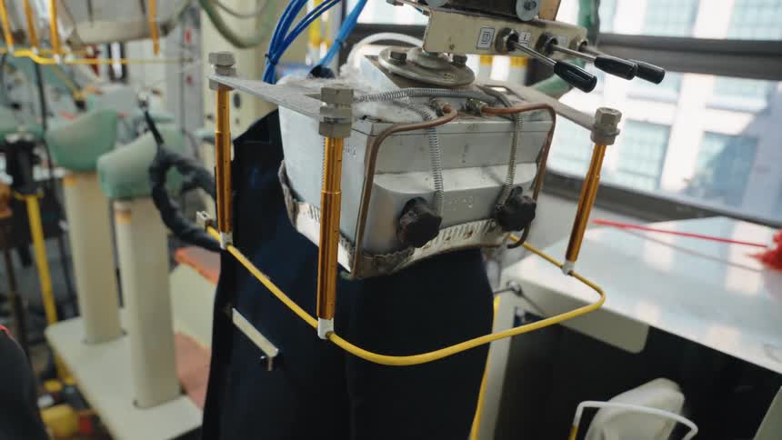 An industrial machine steam presses the shoulder and collar of a jacket at a dry cleaner