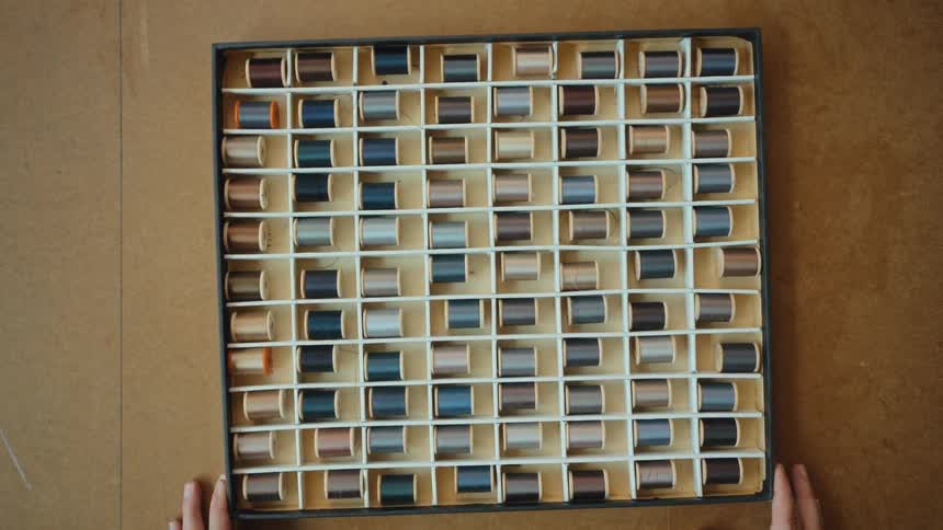 Overhead shot of a person placing a compartmentalized box filled with spools of thread on a wooden surface