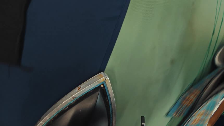 A unique first-person perspective of a tailor ironing various pieces of fabric on a cluttered workbench