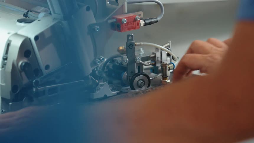 Close-up of a worker's hands guiding fabric through a specialized industrial sewing machine in a textile factory