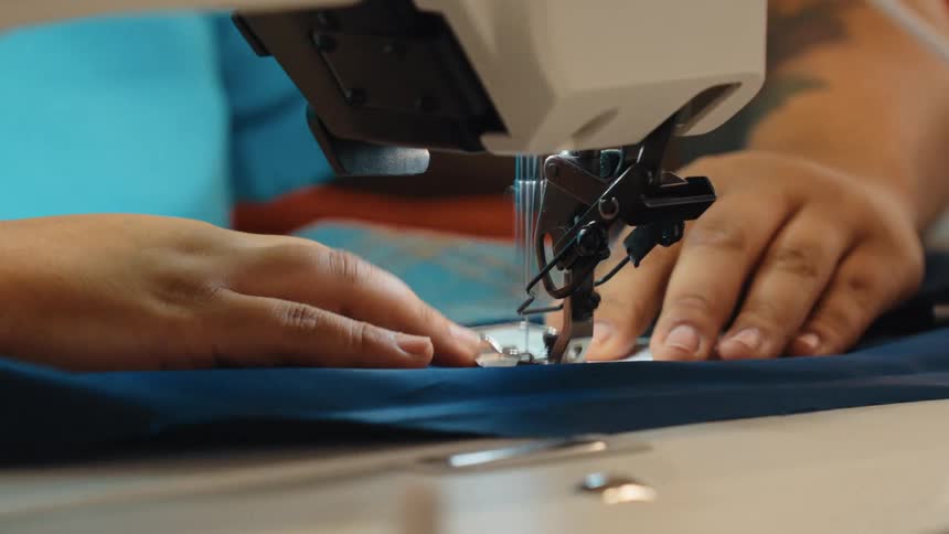 Close up shot of a seamstress expertly guiding blue fabric through a fast-moving sewing machine